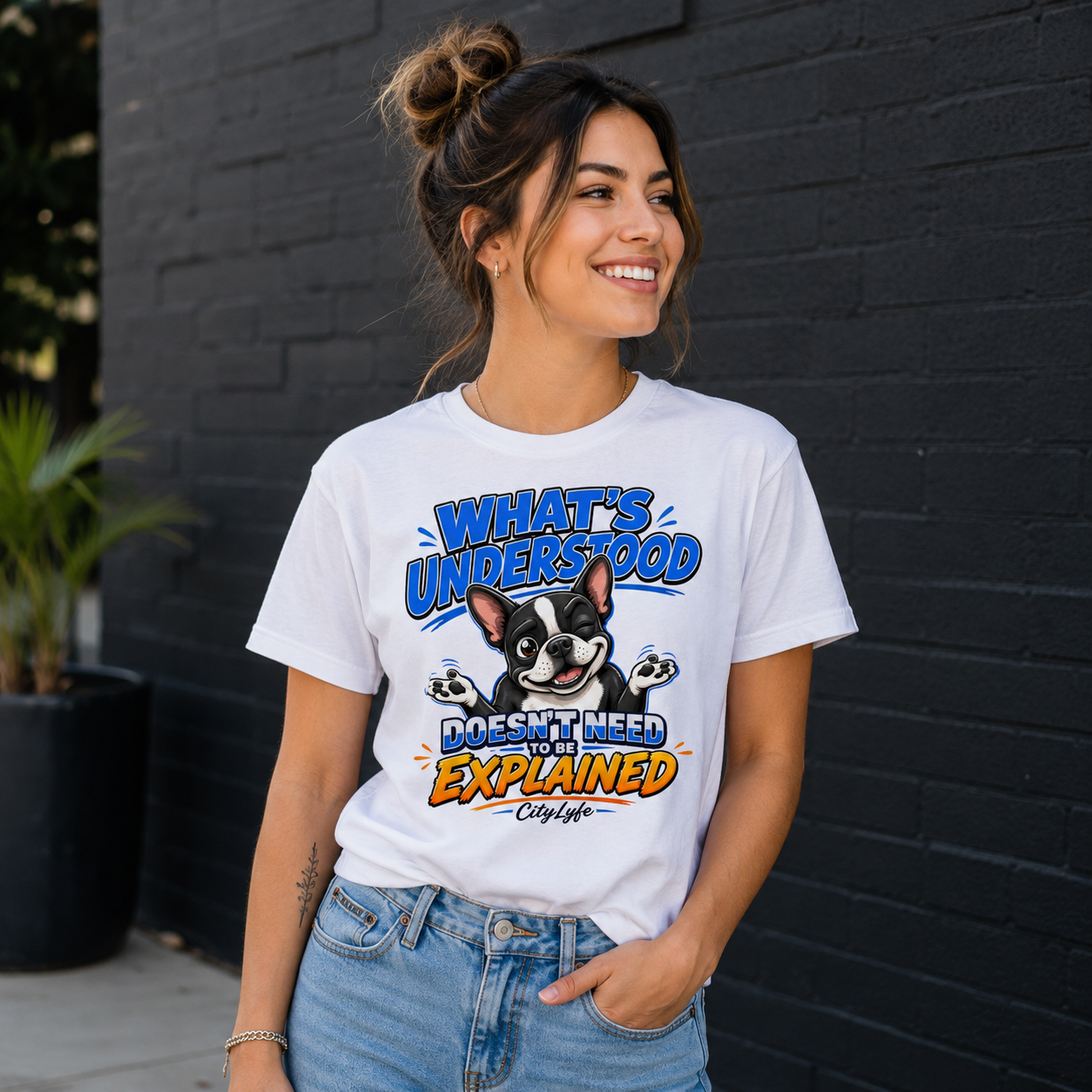 Woman wearing a white t-shirt with a graphic design of a dog and text, standing against a black brick wall.